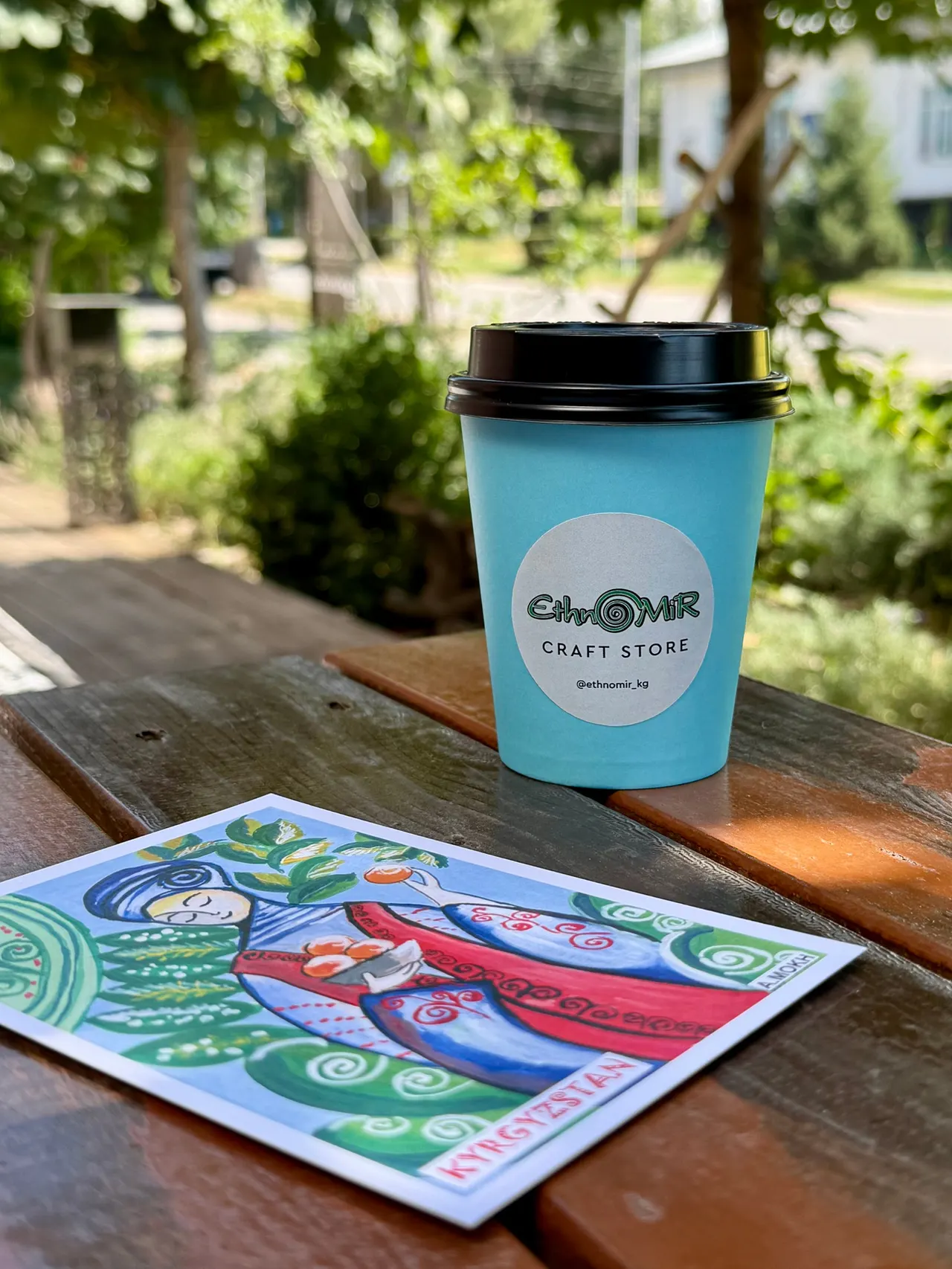 An EthnoMir coffee cup and a postcard on a veranda table