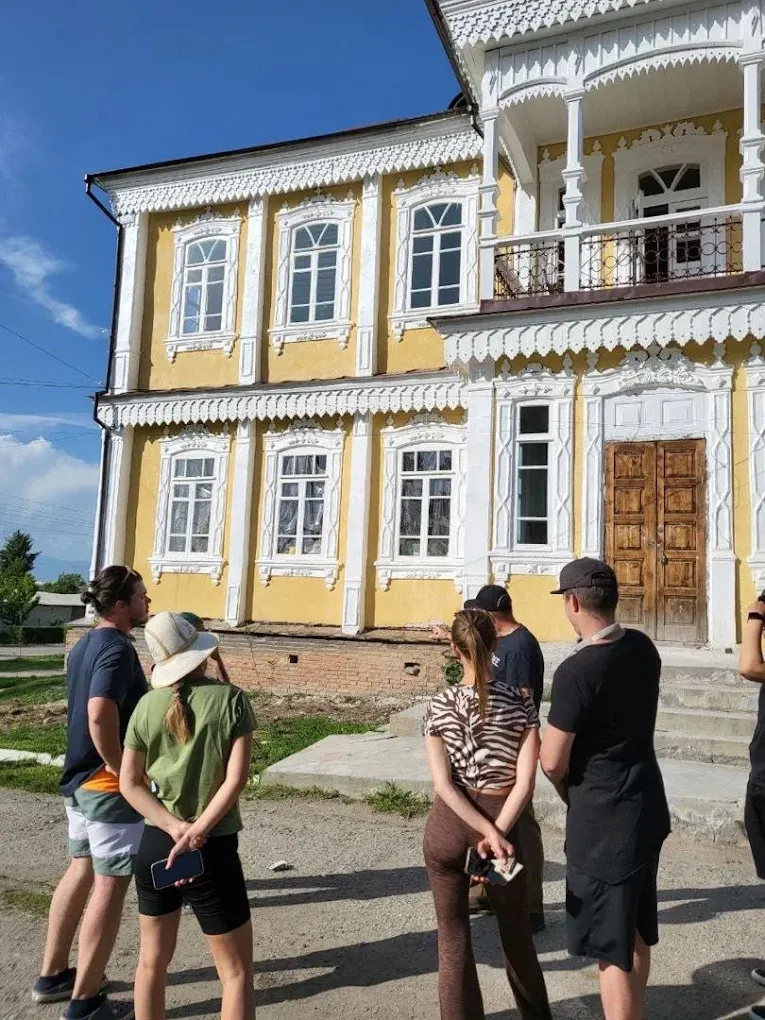 Tour guests at a yellow merchant house with a carved balcony in Karakol